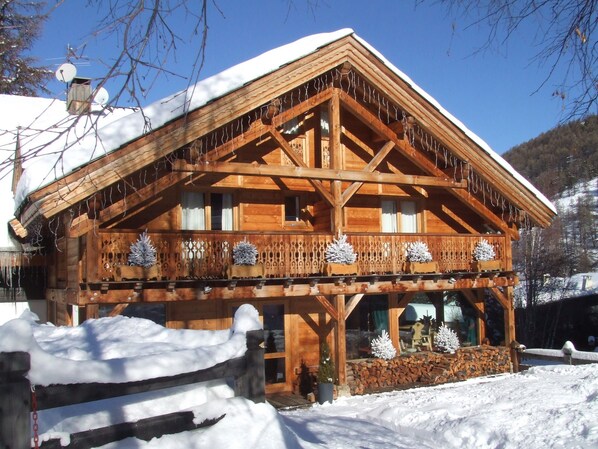 Una cabaña de madera con balcón, techo cubierto de nieve y piñas decorativas.