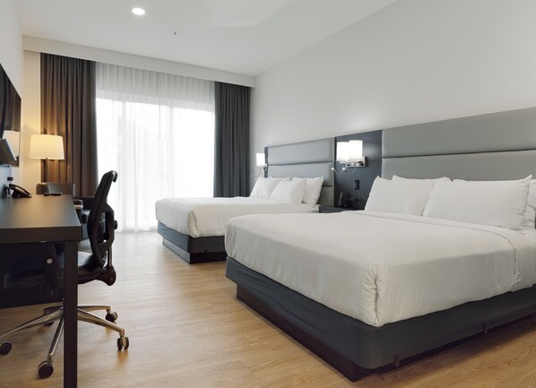 A hotel room with two beds, a desk with a lamp, a chair, and a large window with curtains. - Hôtel Rive Gauche (Beloeil)