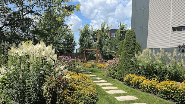 A garden pathway with stepping stones, surrounded by various flowering plants and trees.