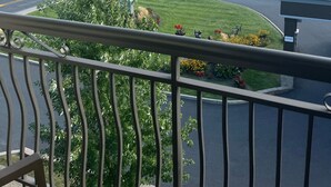 A balcony with a view of a road, a parking lot, and a body of water with mountains in the background.