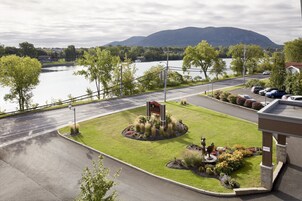 Entrada de hotel con jardín ajardinado, una señal y vistas a un lago y montañas.