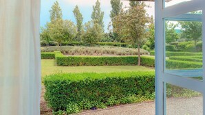 Vista de dentro de um edifício para um jardim bem cuidado, com sebes e árvores podadas.