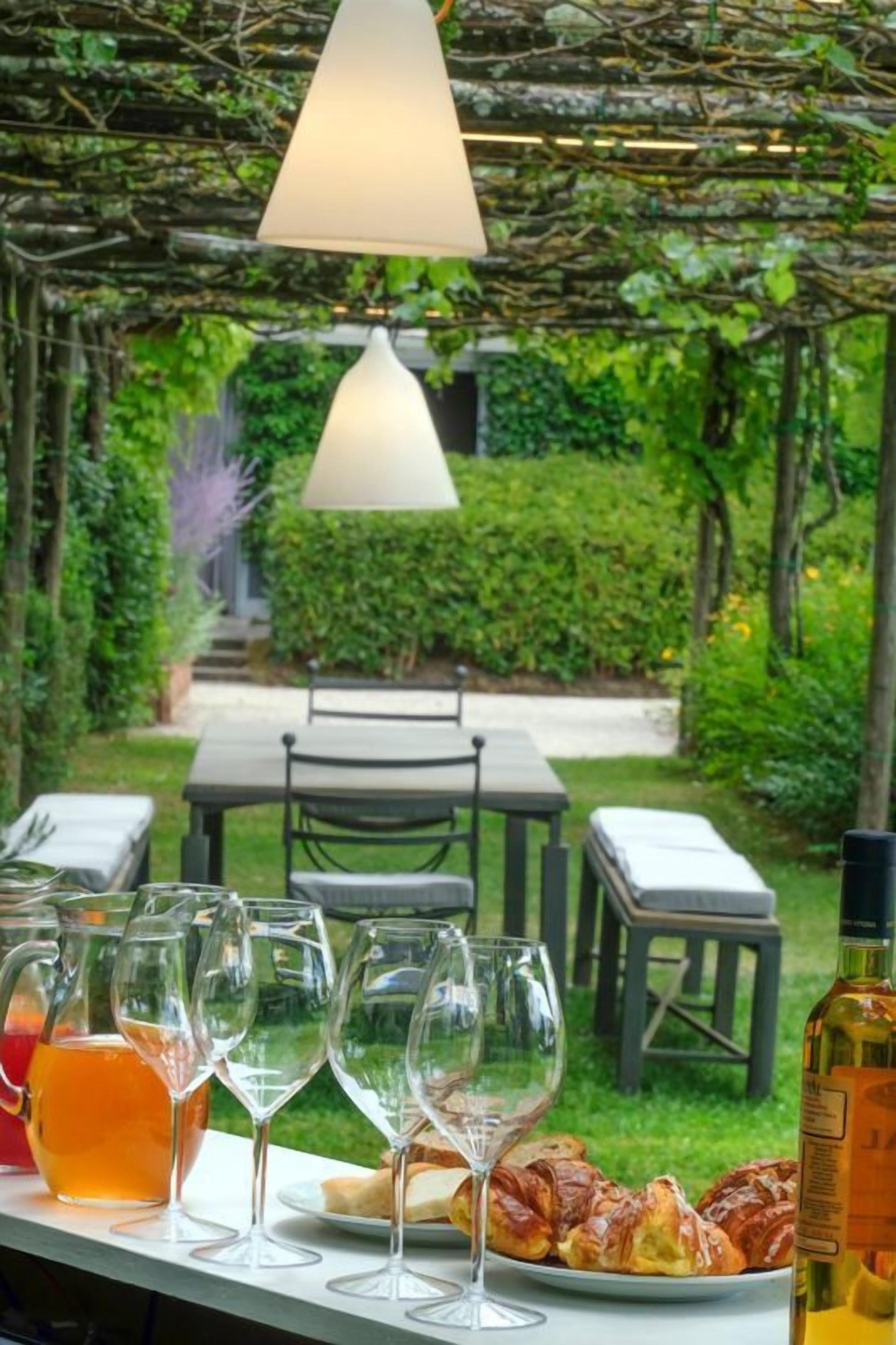 An outdoor dining area with a table set for a meal, including a bottle of wine, glasses, and a pitcher of orange juice.