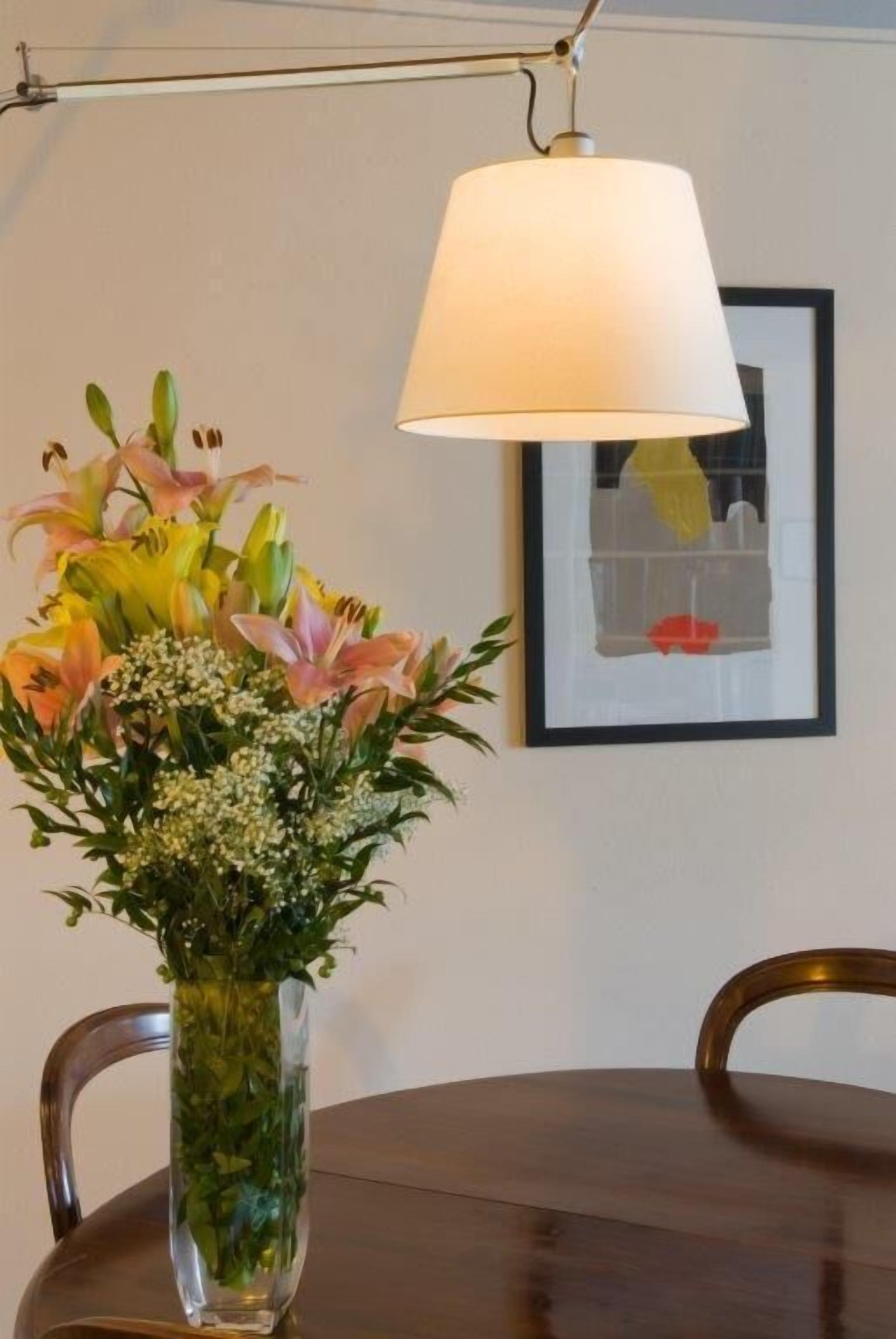 Une table à manger ornée d’un vase de fleurs, d’une lampe et d’un tableau encadré accroché au mur.