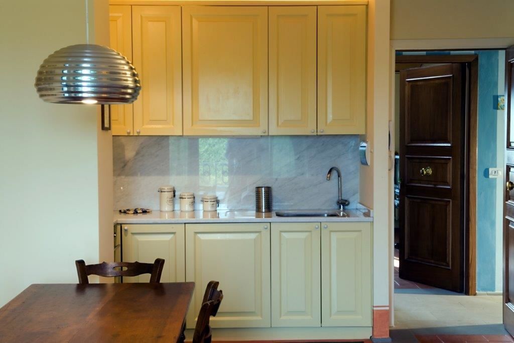 A kitchen with light-colored cabinets, a marble backsplash, and a stainless steel sink. There is a wooden dining table with chairs.