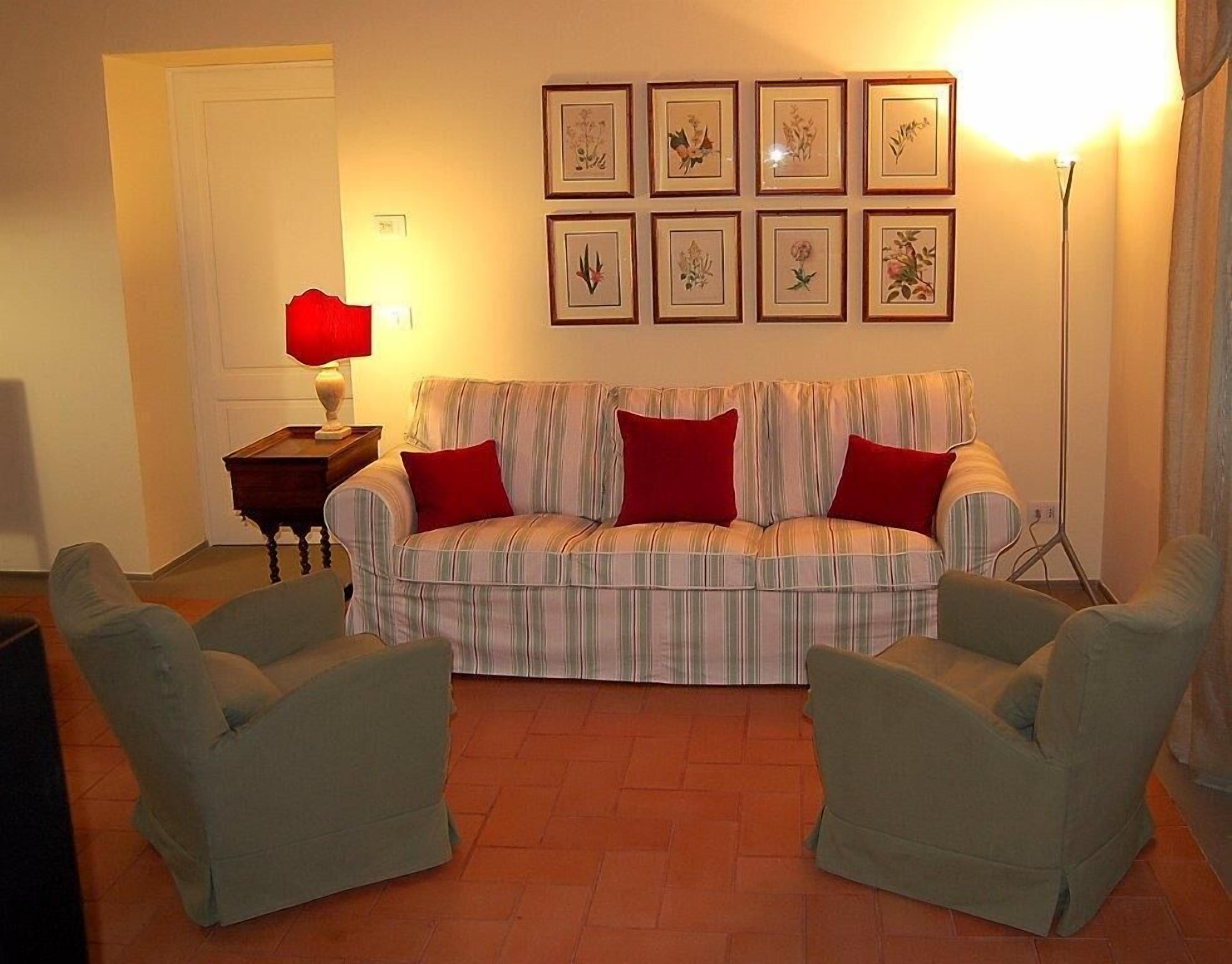 A living room with a striped sofa, two armchairs, a red lamp, and framed botanical prints on the wall.