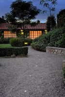 Una casa con camino de grava que conduce a una entrada con baldosas, rodeada de setos cuidados y un árbol grande.