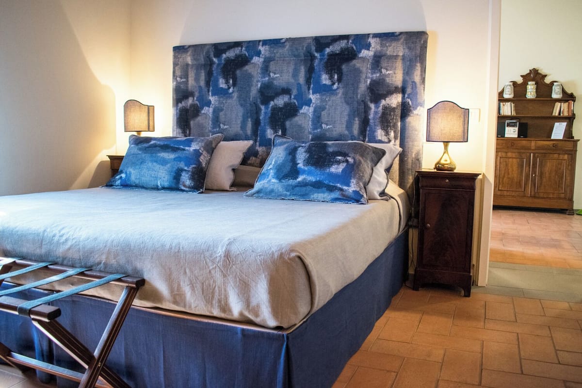 A bedroom with a large bed, two bedside tables, a nightstand, and a wooden cabinet in the background.