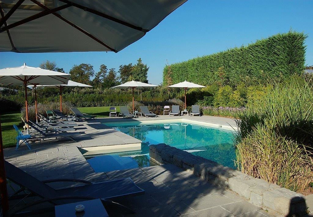 Zwembad met ligbedden en parasols, omringd door een aangelegde tuin.