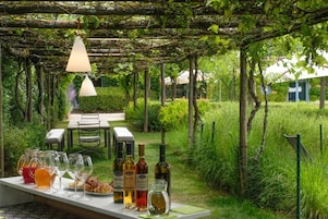 An outdoor dining area with a table set for two, surrounded by lush greenery and a pergola overhead.