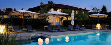 Zona de piscina con sillas de descanso y sombrillas, piscina e inmueble con tejado de azulejos.