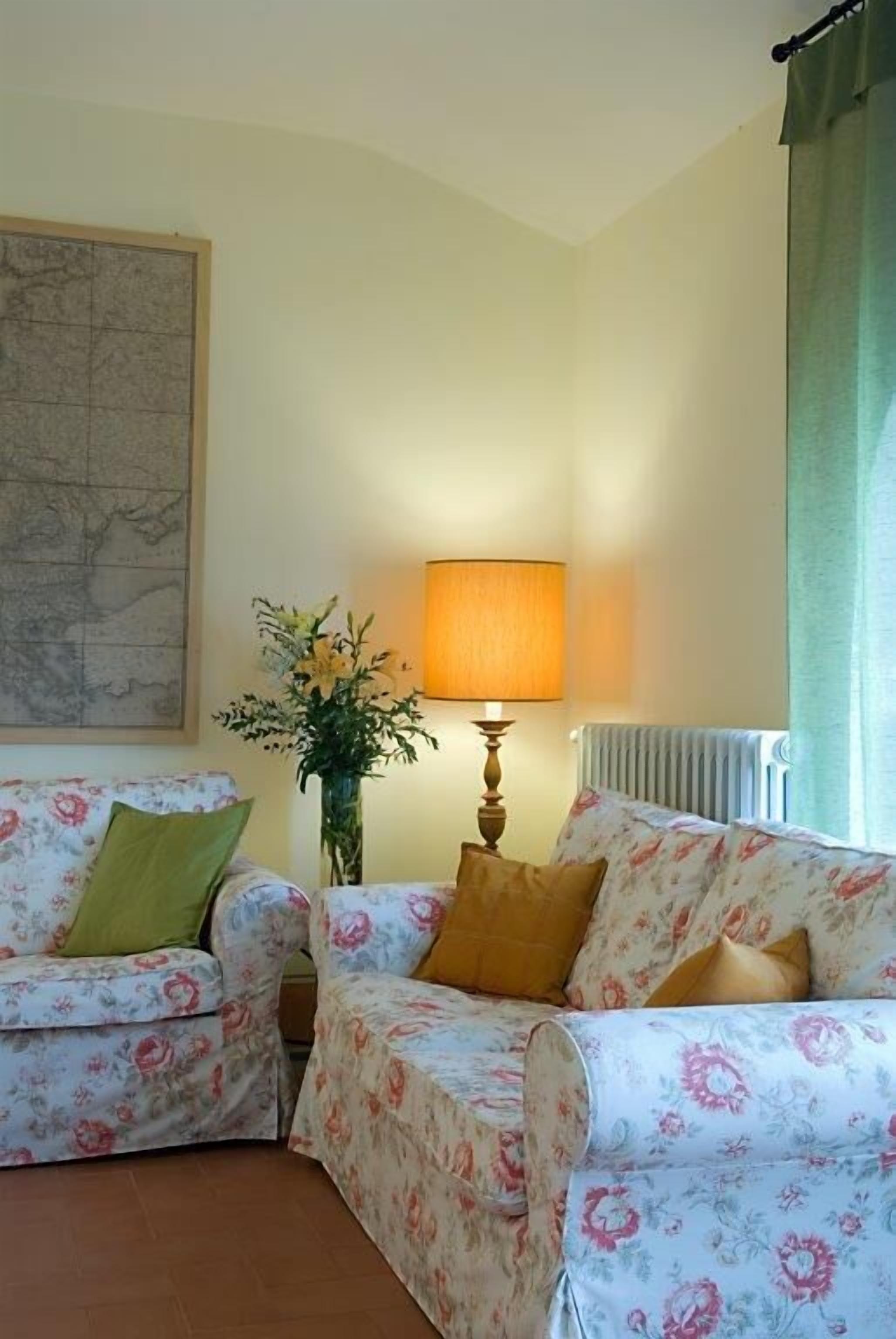 Uma sala de estar com dois sofás de padrão floral, um abajur, um vaso com flores e um mapa na parede.