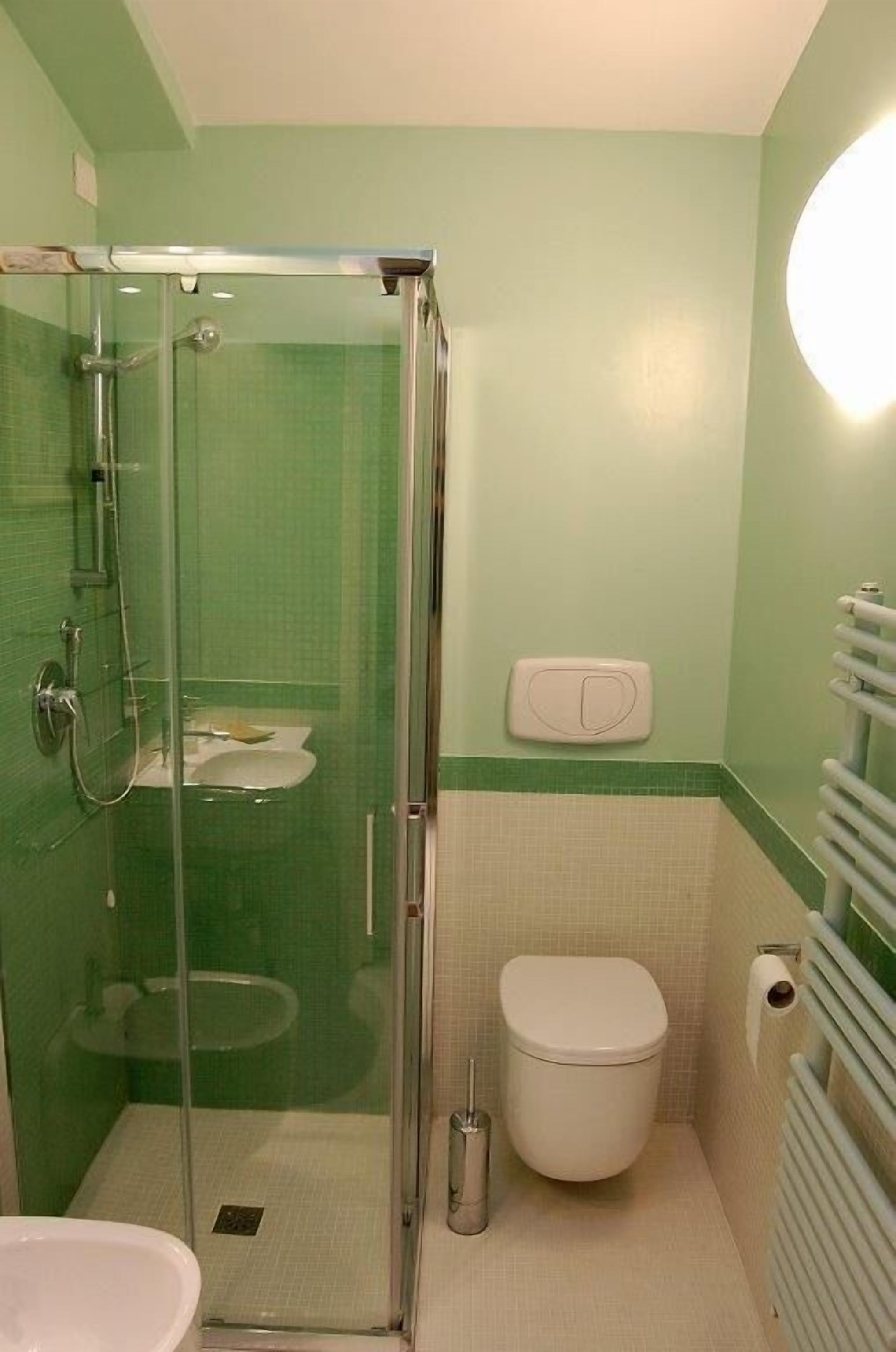 Et badeværelse med en glasafskærmet brusekabine, toilet, håndvask og et håndklædestativ.