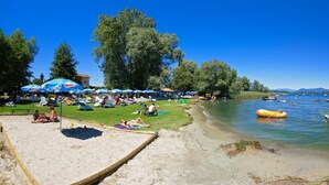 Una playa con gente tomando el sol, nadando y barcos en el agua.