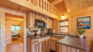 Interior de una cabaña de madera con cocina, una cama y comedor.