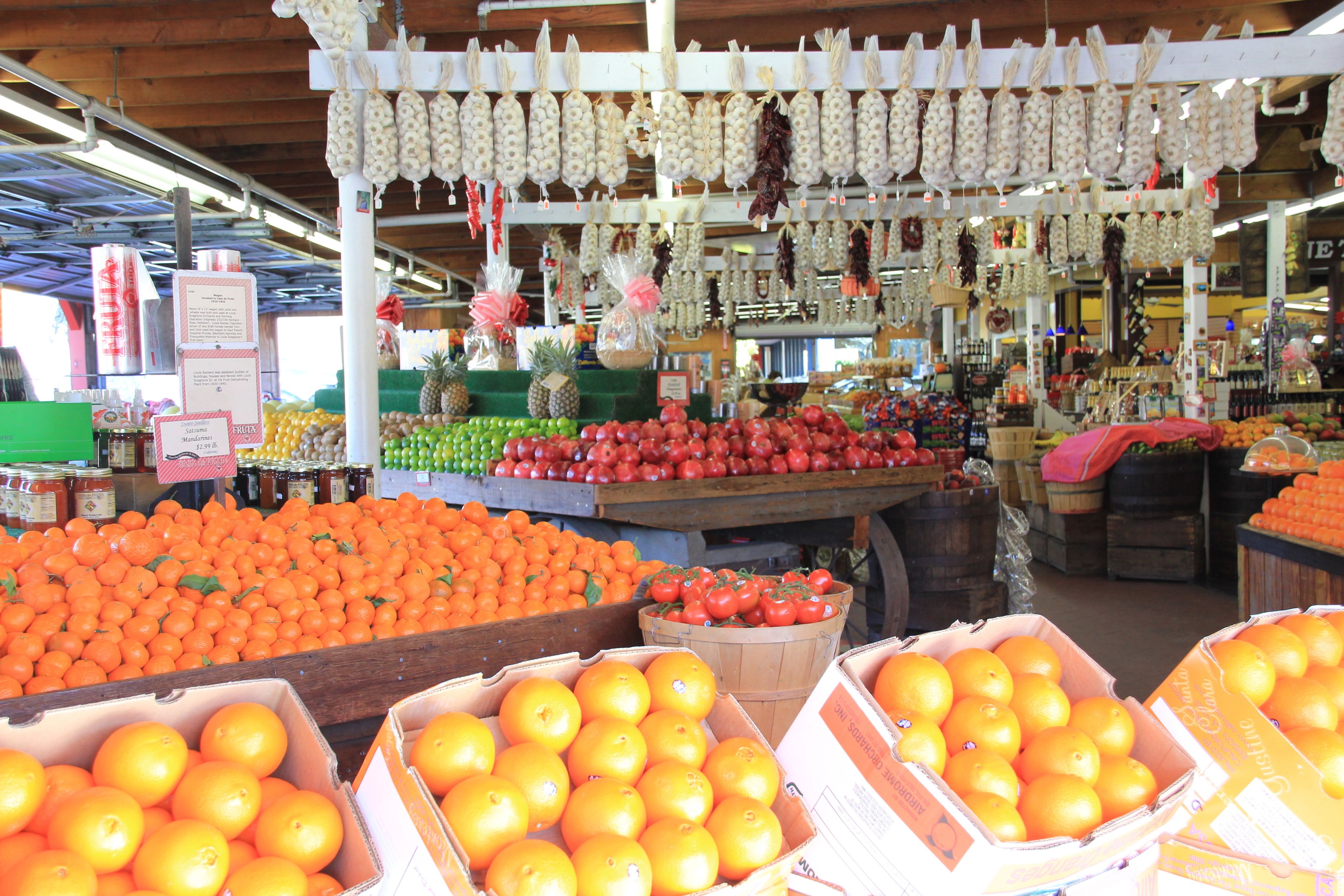 A market with various fruits and vegetables, including oranges and tomatoes, displayed in boxes and baskets.