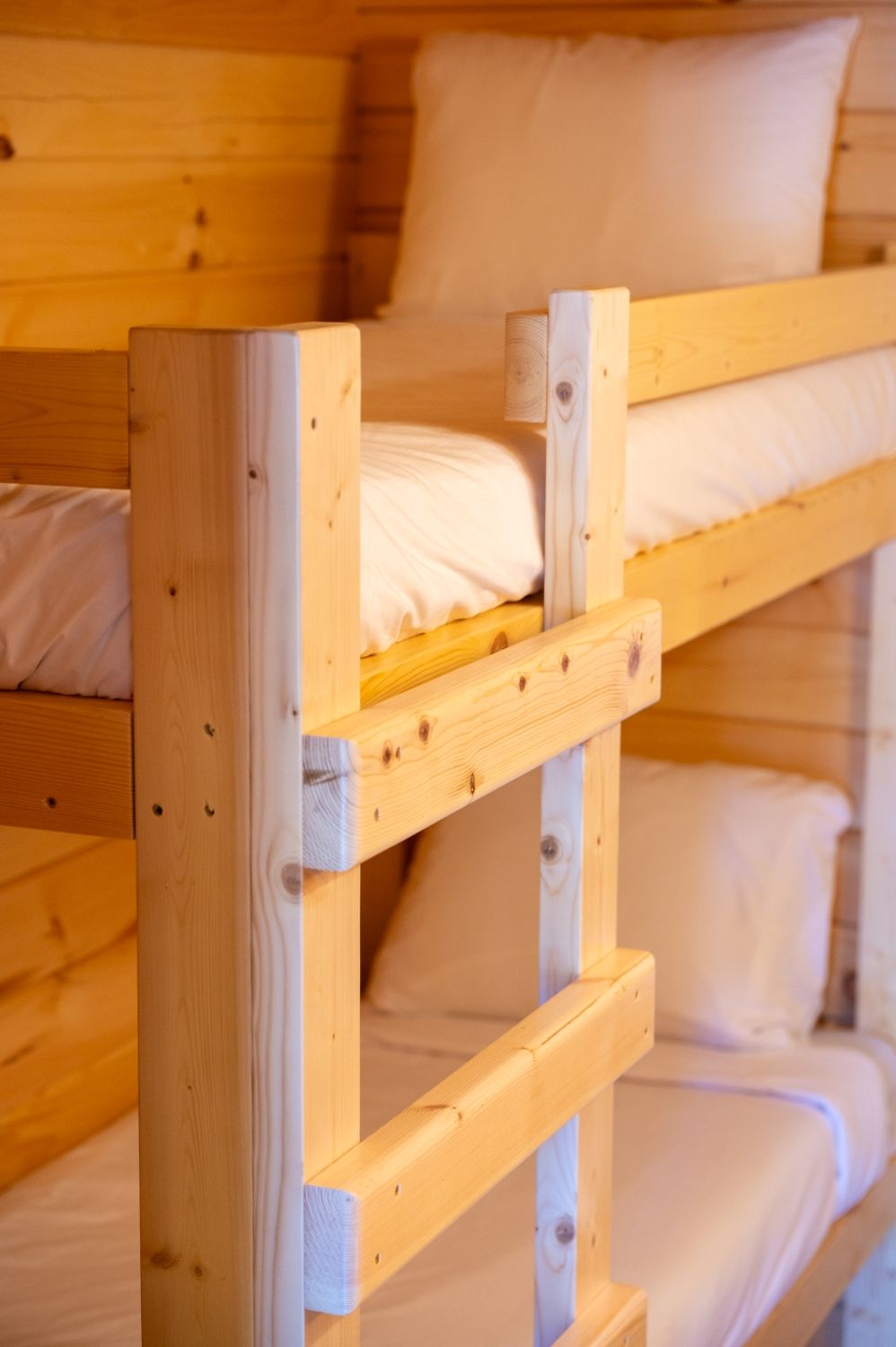 A bunk bed with wooden frames and white bedding.