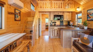 Interior de una cabaña de madera con cocina, comedor y una escalera que sube a un altillo.