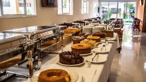 Montaje de bufé con diversos alimentos, incluyendo pasteles y repostería, dispuesto sobre una larga mesa con utensilios y platos.