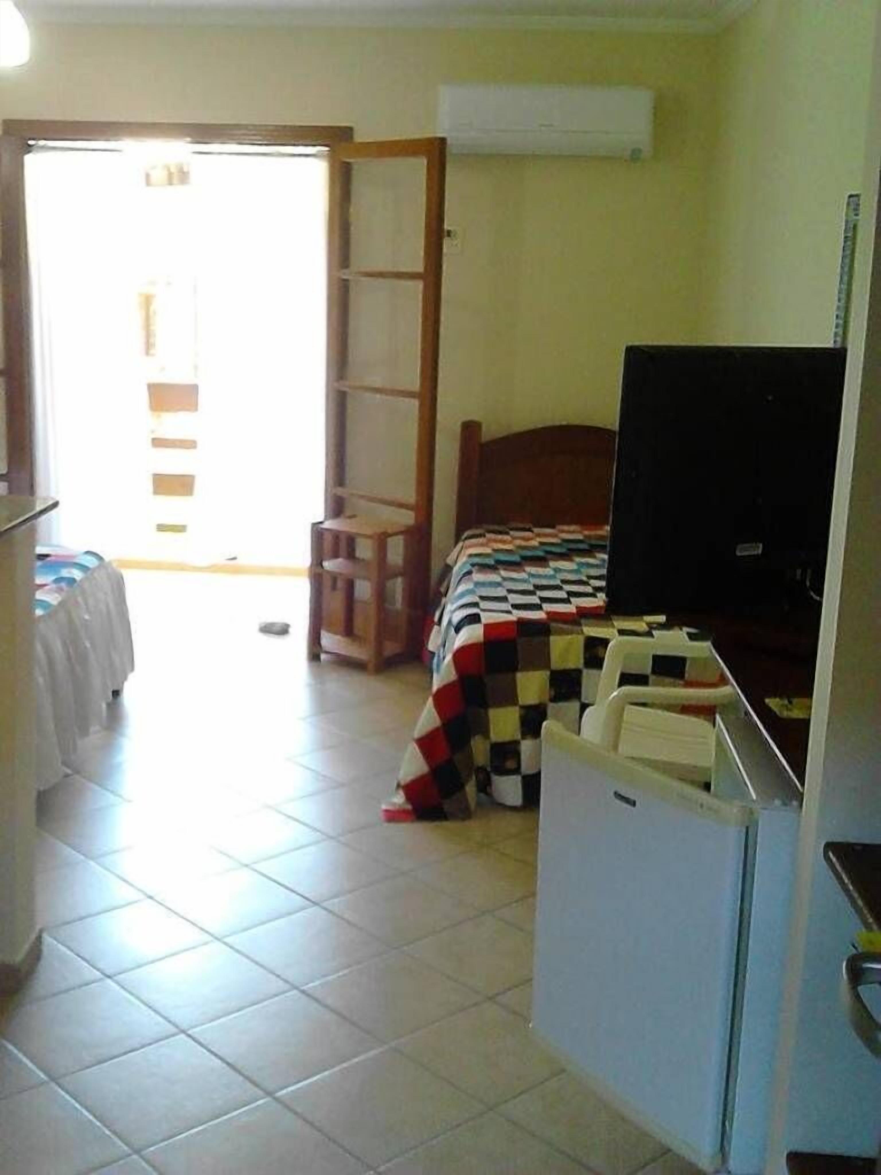 A room with a bed, a television, a desk, and a chair. There is a door leading to another room.
