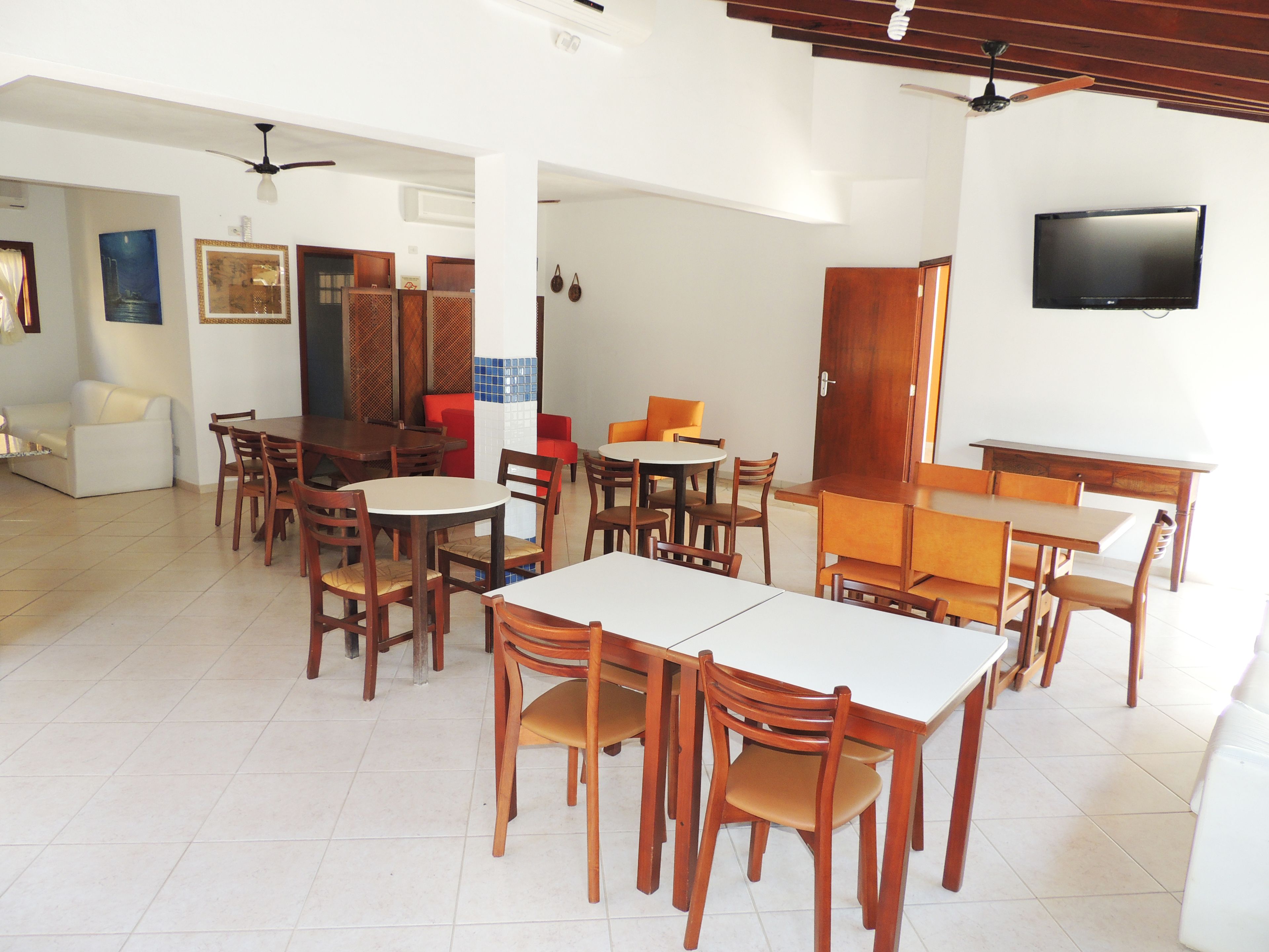 A dining area with multiple tables and chairs, a television mounted on the wall, and a ceiling fan.