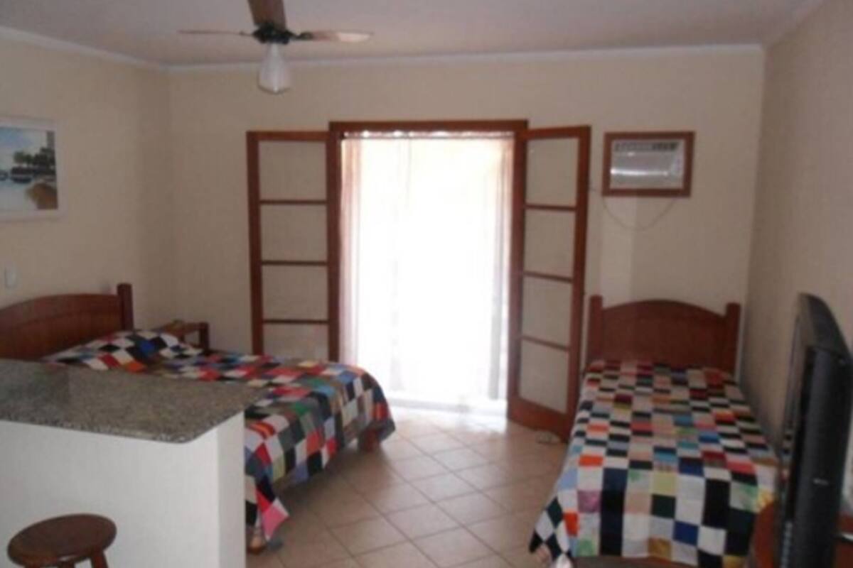A room with two beds, a ceiling fan, a window, and a television.