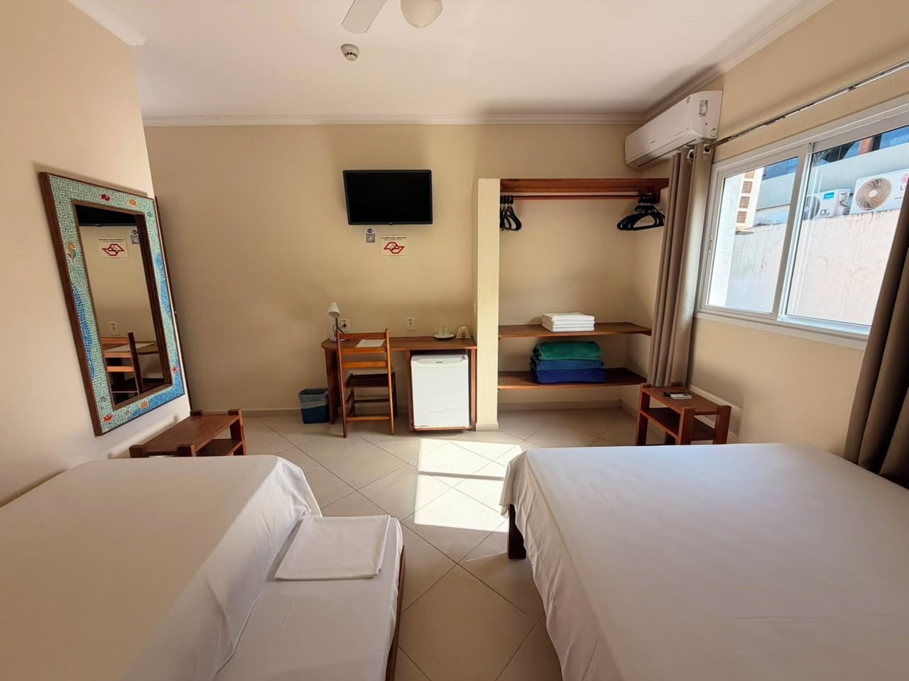 A hotel room with two beds, a desk, a television, and a window with curtains.