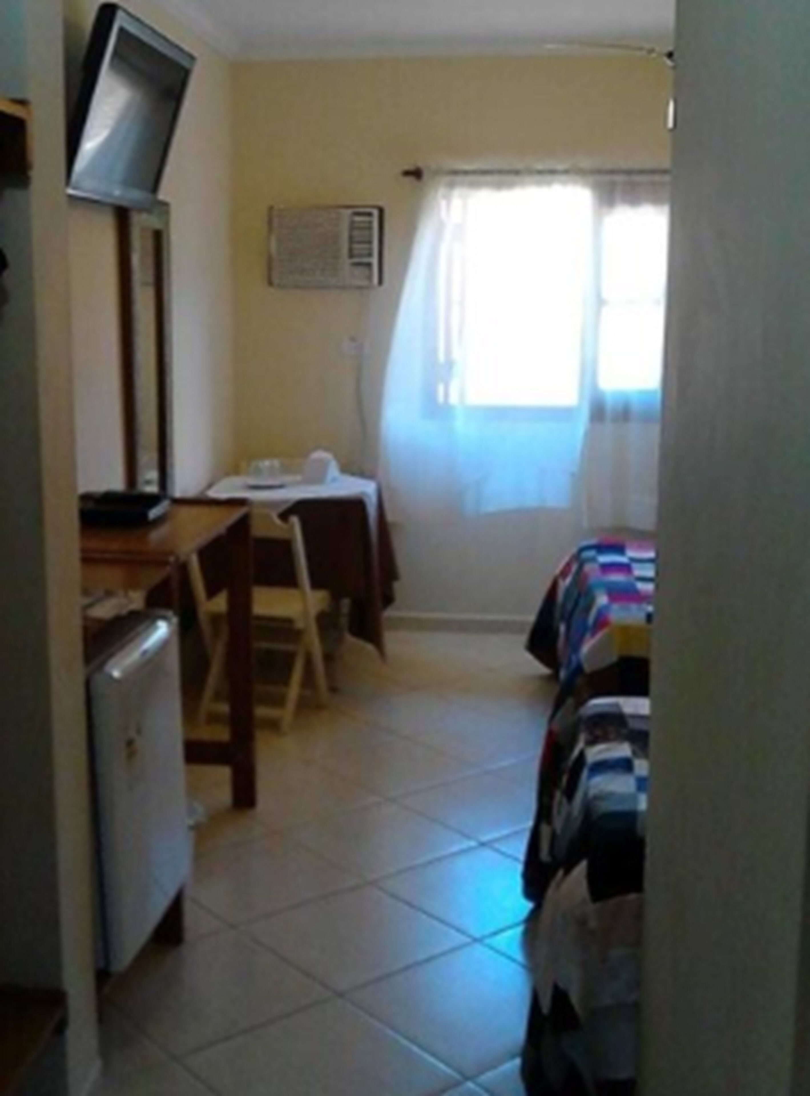 A small, compact room with a bed, a desk, a chair, and a television.