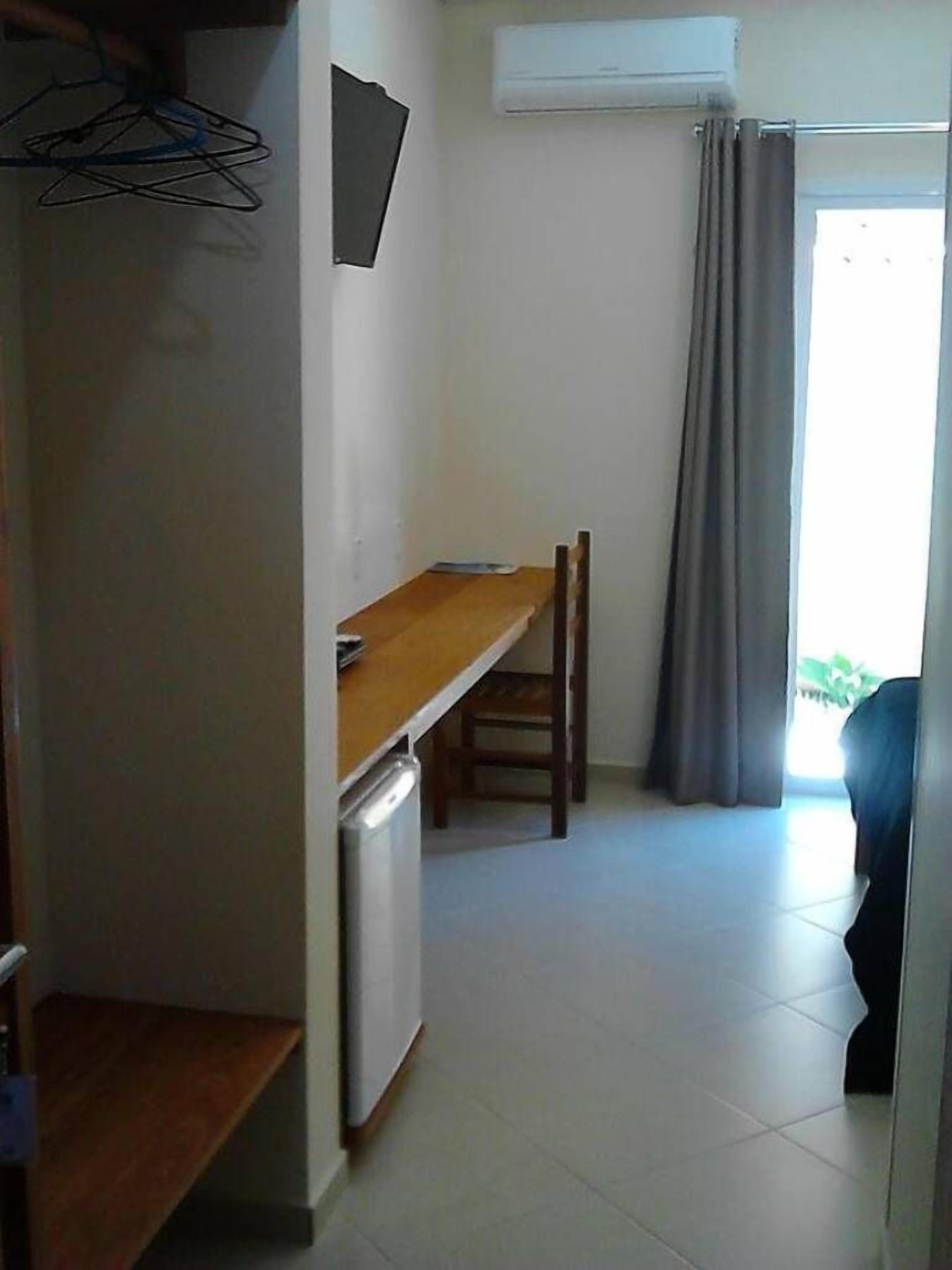 Un pasillo estrecho con una mesa de madera y sillas, un refrigerador pequeño y una ventana con cortinas.