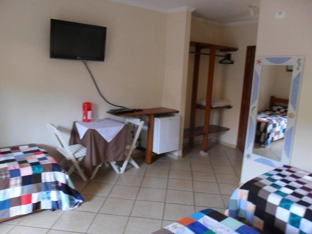 Une chambre avec deux lits, une petite table avec une chaise, un téléviseur fixé au mur et une armoire.