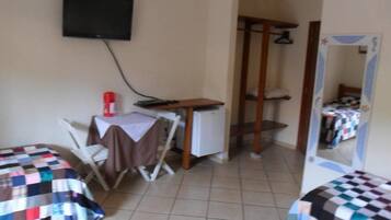 Une chambre avec deux lits, une petite table avec une chaise, un téléviseur fixé au mur et une armoire.