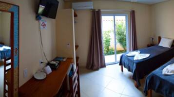 Quarto de hotel com escrivaninha, duas camas, televisão e porta de correr para uma varanda.