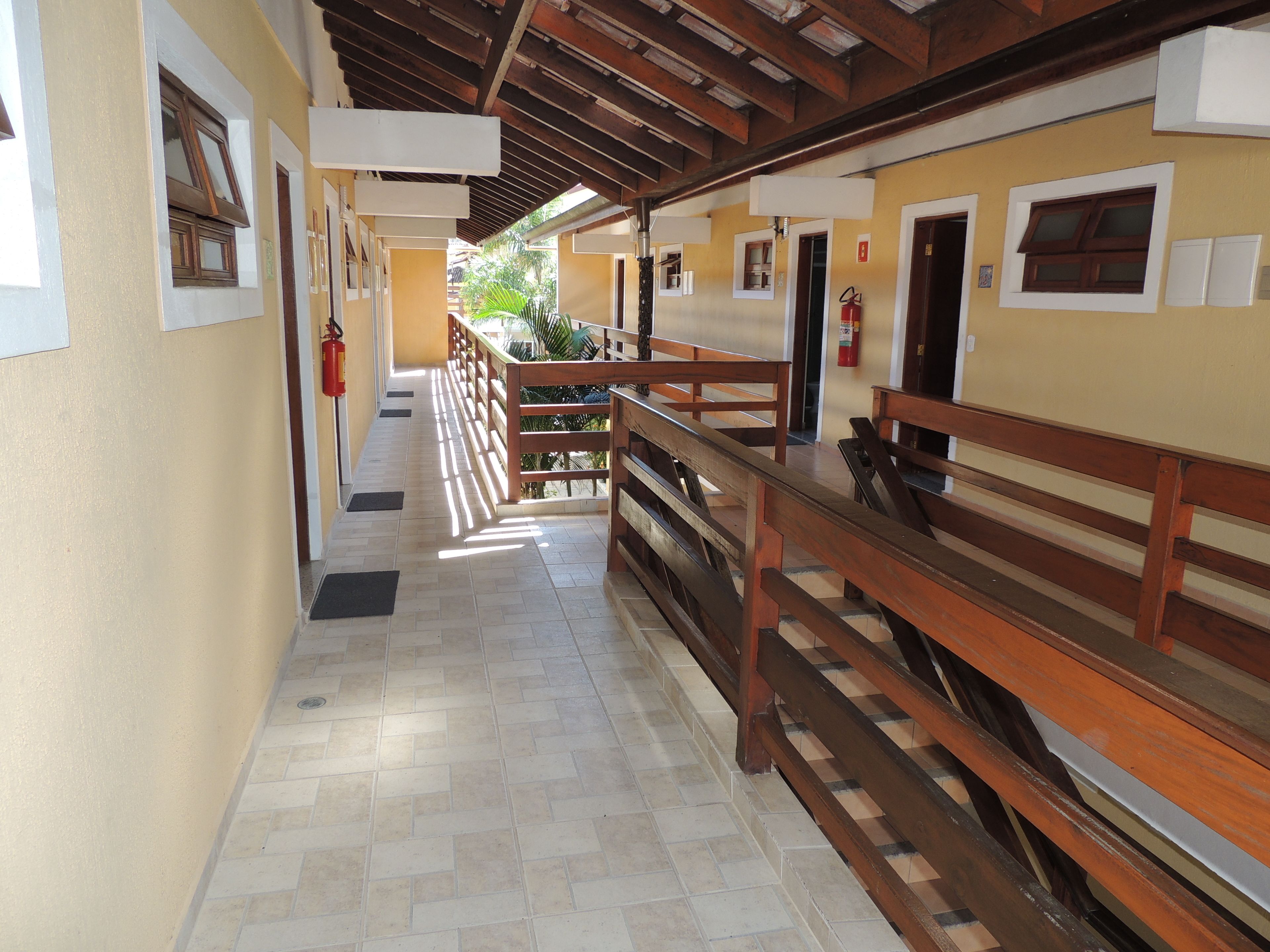 A corridor with wooden benches, a tiled floor, and a covered area with a wooden ceiling.