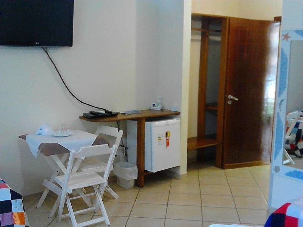 A small room with a dining table, chairs, a refrigerator, and a TV mounted on the wall.
