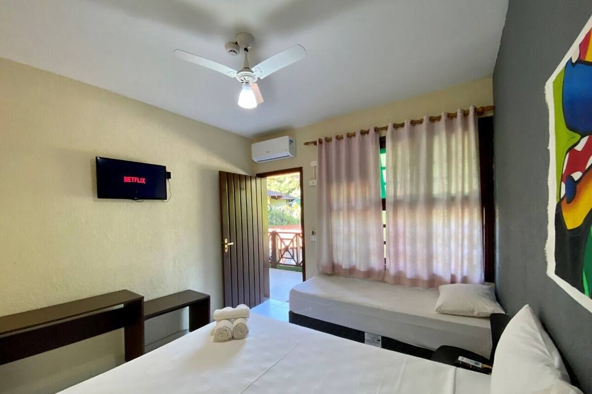 A hotel room with a bed, a TV mounted on the wall, a ceiling fan, and a window with curtains.