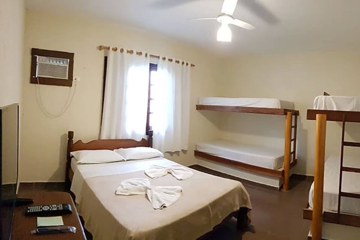 A single bed with a wooden headboard, a bunk bed, a desk with a chair, and a ceiling fan.