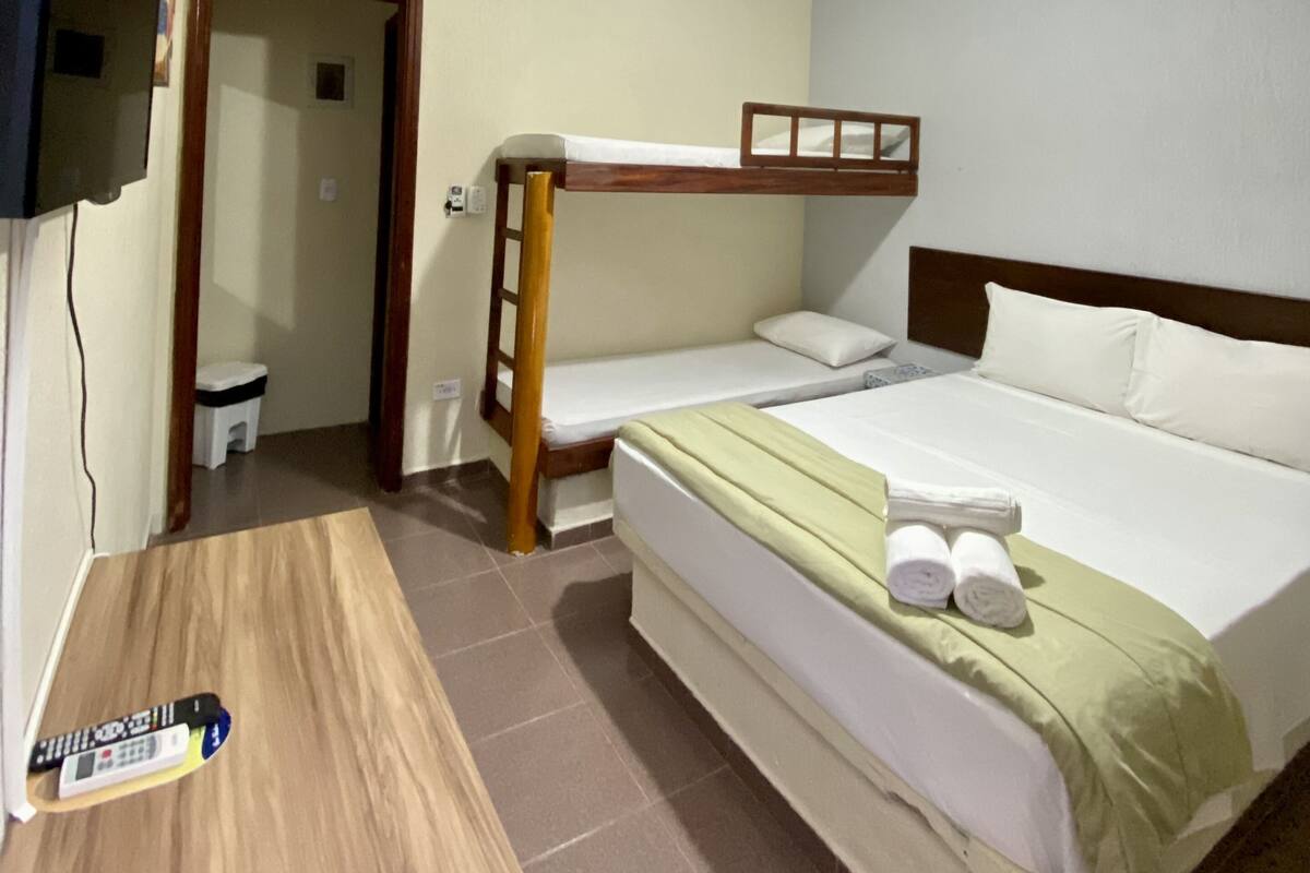 A room with bunk beds, a ceiling fan, a TV mounted on the wall, and a small table with a remote control.