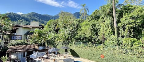 A swimming pool with a herringbone tile pattern, surrounded by a deck with outdoor furniture and a view of lush greenery and mountains.