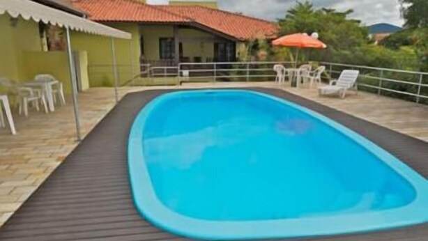 A rectangular swimming pool with a dark deck, surrounded by a white fence and outdoor furniture. - Pousada Mariane (Bombinhas)