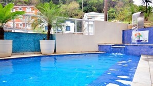 A swimming pool with clear blue water, surrounded by potted plants and a tiled edge. - Hotel Guarumar (Guarujá)