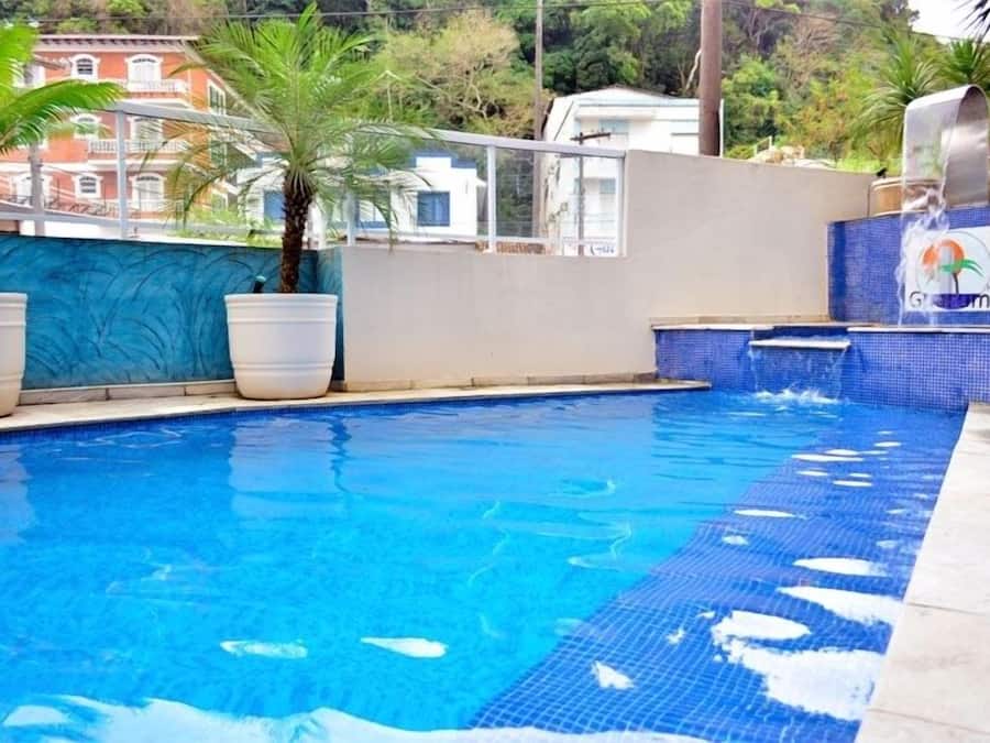 A swimming pool with clear blue water, surrounded by potted plants and a tiled edge.