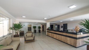 A spacious lobby with a reception desk, seating area, and potted plants. - Hotel Guarumar (Guarujá)
