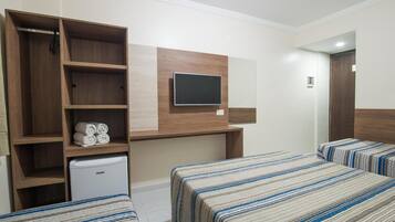 A hotel room with two beds, a TV mounted on the wall, a wardrobe, and a mini-fridge.