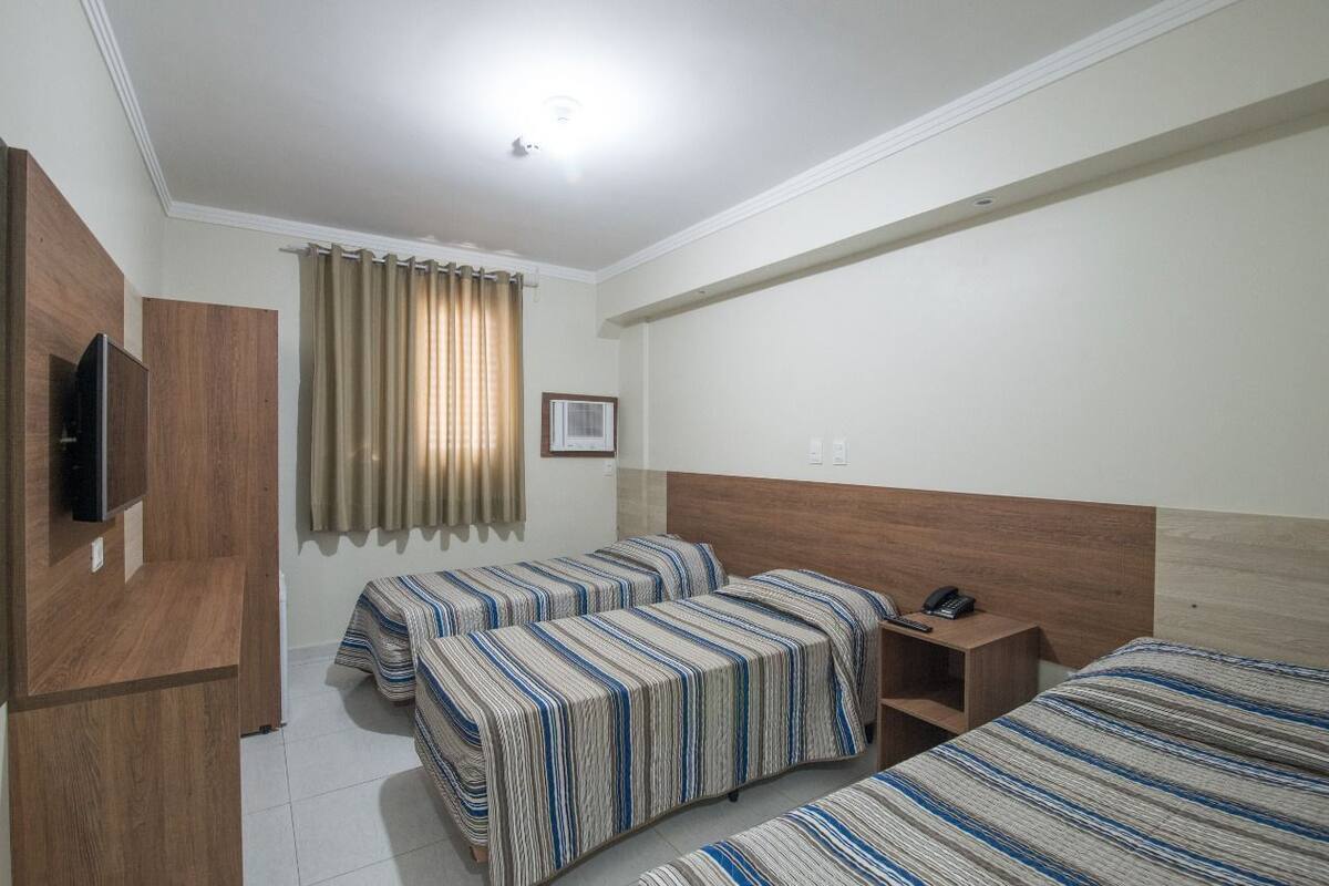A hotel room with two single beds, a wooden headboard, a bedside table with a phone, and a TV mounted on the wall.