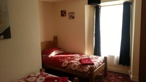A room with two wooden beds, each with floral bedding and red pillows. There is a window with dark curtains, and a small wall-mounted picture frame. - The Vyvyan Arms Hotel (Camborne)