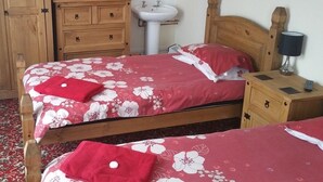 Un dormitorio con dos camas, un armario de madera, una mesita de noche con lámpara y un mueble auxiliar.