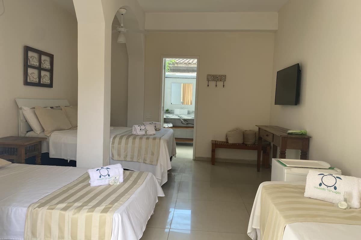 Quarto de hotel com duas camas, televisão, mesa pequena e um banquinho.