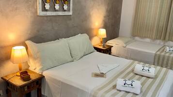 Habitación de hotel con dos camas, cada una con cubrecama a rayas y un par de toallas con un logotipo. En la pared, un cuadro de flores, una mesita de noche con una lámpara y una ventana con cortinas.