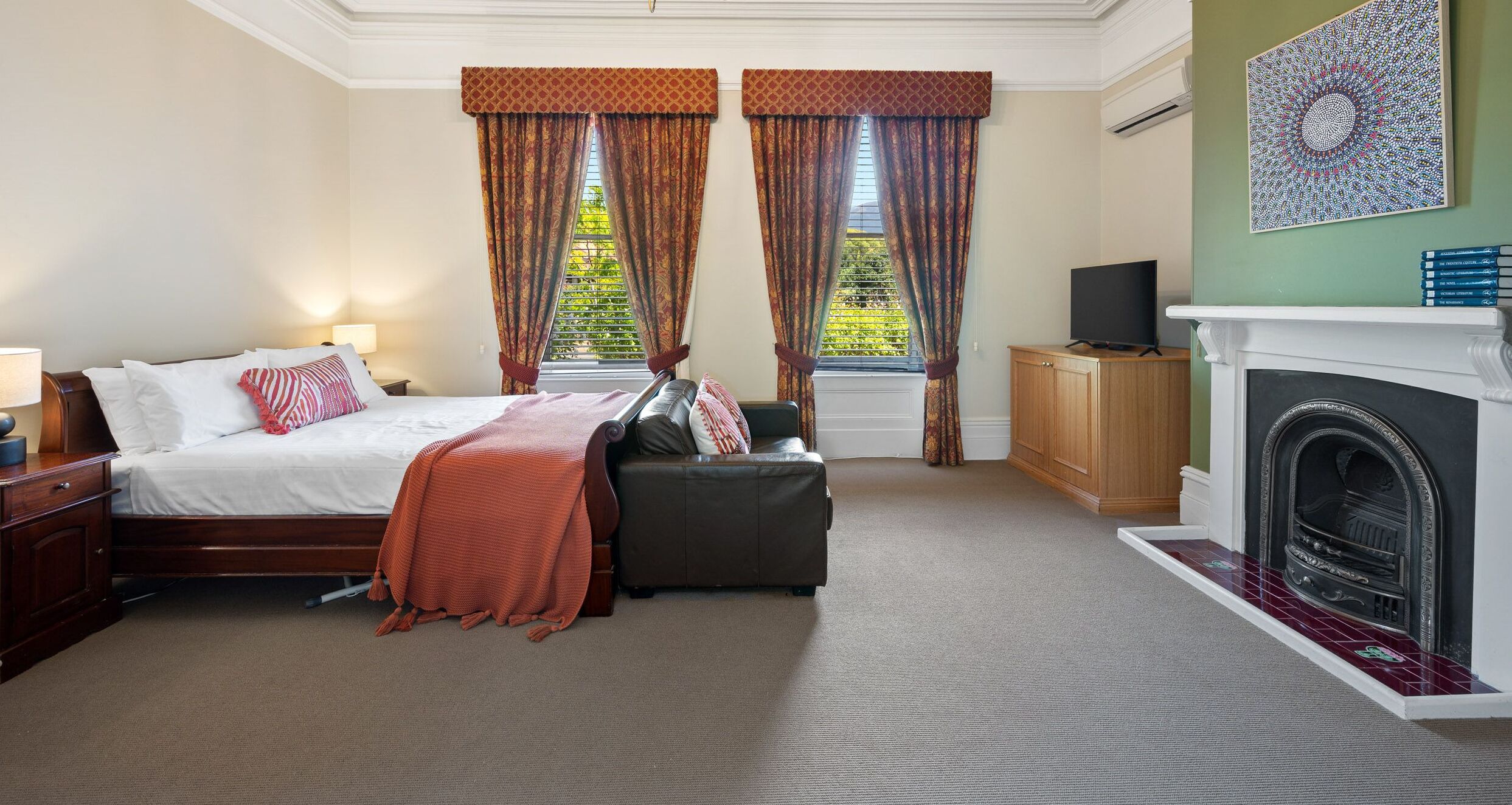 A hotel room with a bed, a sofa, a television, a fireplace, and a window with curtains.