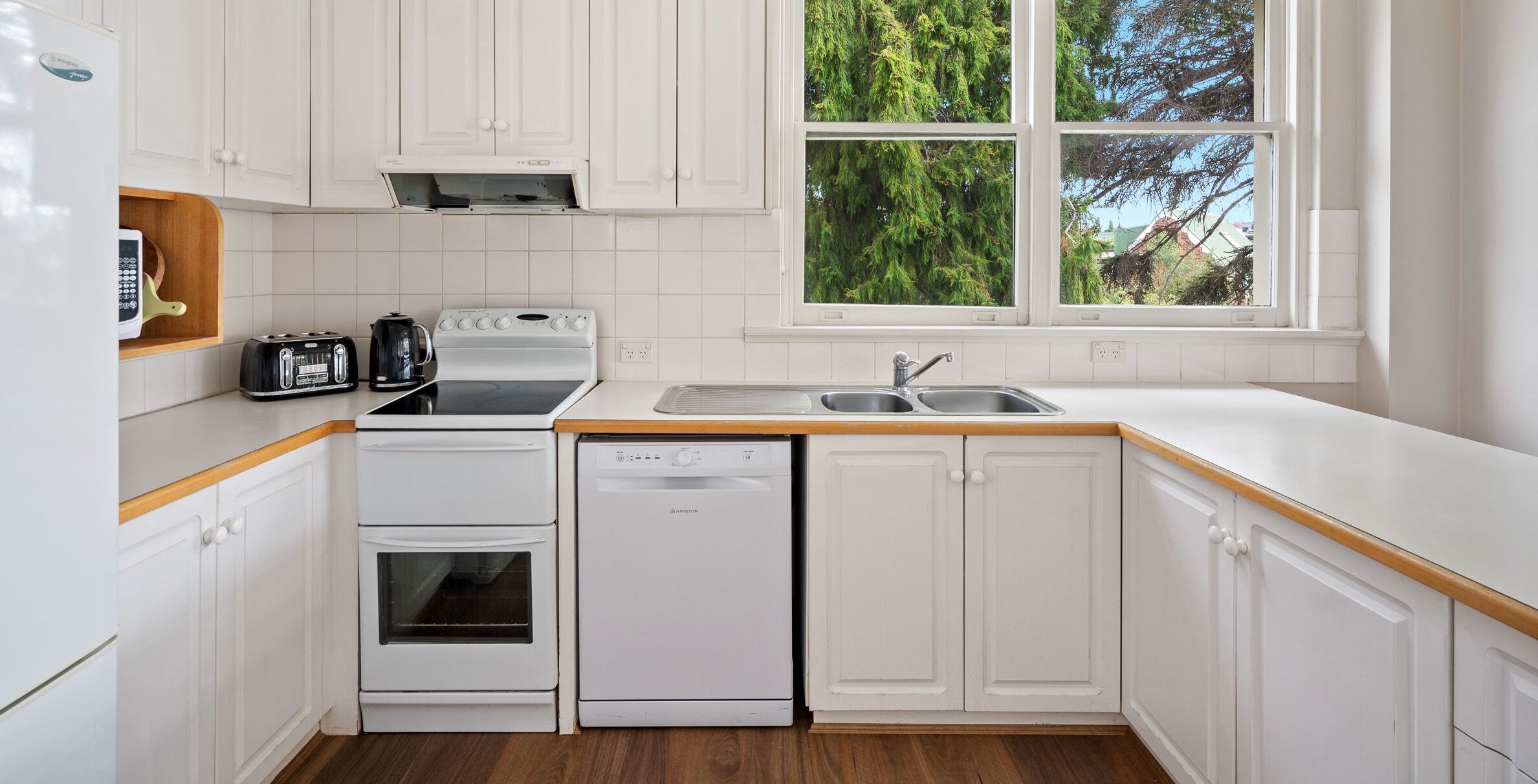 Een moderne keuken met witte kasten, een vaatwasser, een kookplaat en een spoelbak.